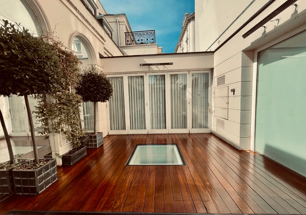 Freshly sanded and oiled rooftop timber deck in East Barnet, rich brown boards surrounding a central glass skylight within a bright courtyard.