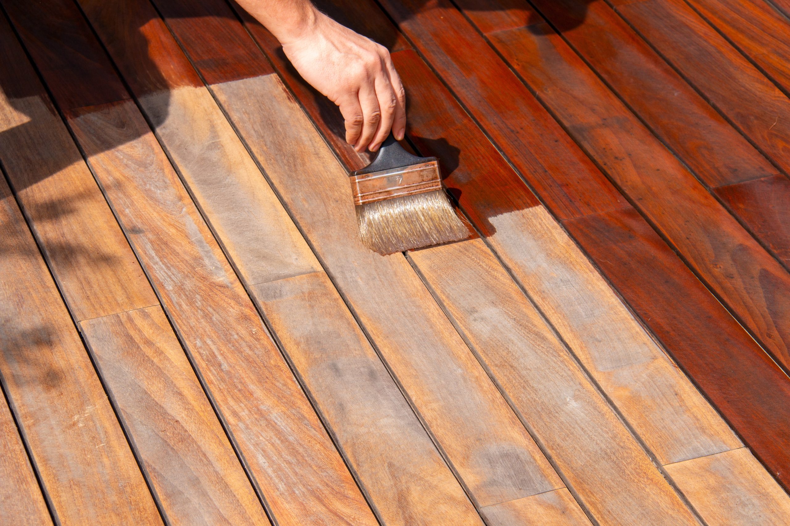 Close-up of a hand brushing protective oil onto freshly sanded deck boards in East Barnet, highlighting the rich colour change after deck sanding.
