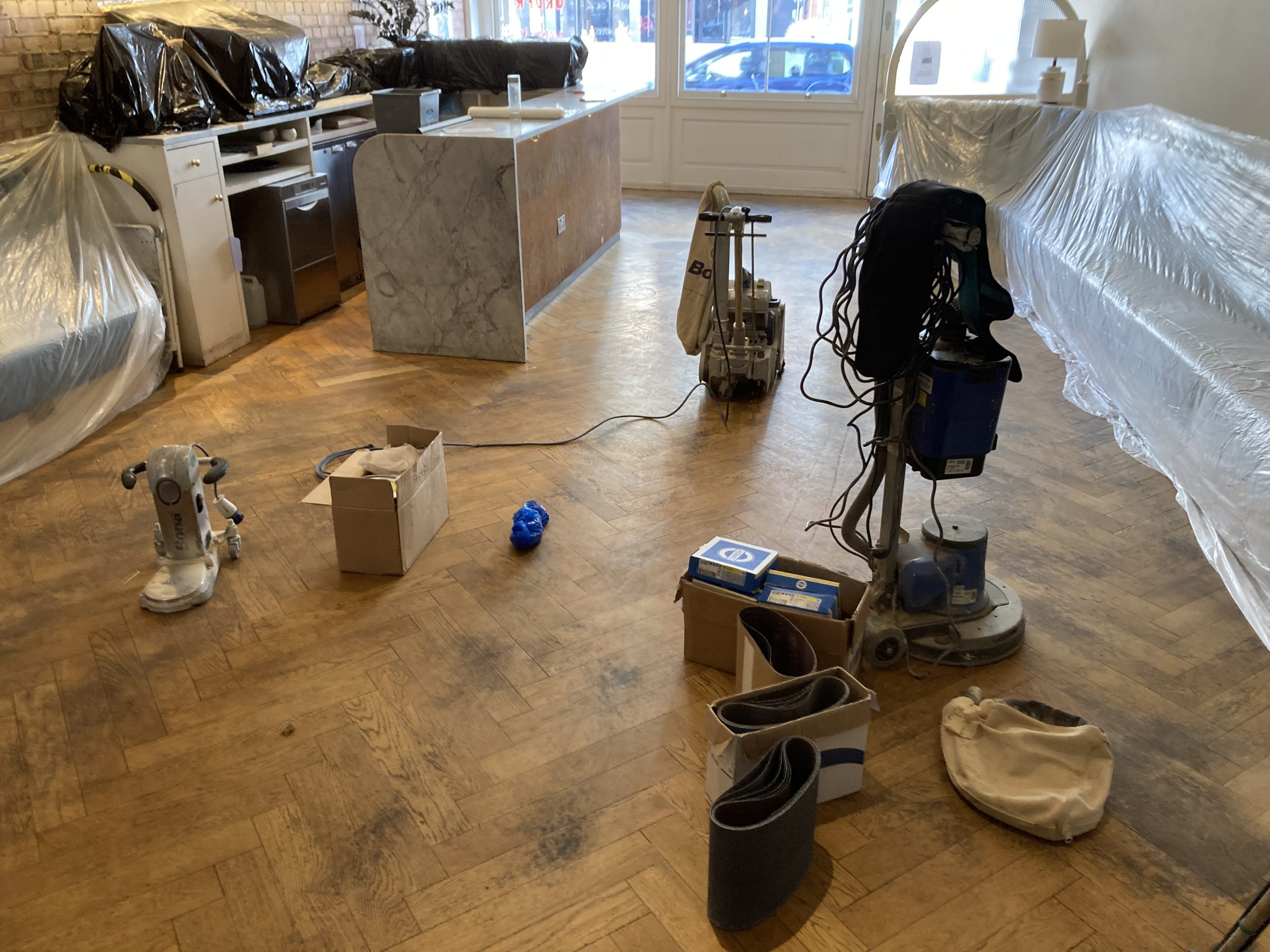 Professional sanding machines and tools set up on an oak herringbone parquet floor before restoration — Herringbone Parquet Sanding preparation in East Barnet.