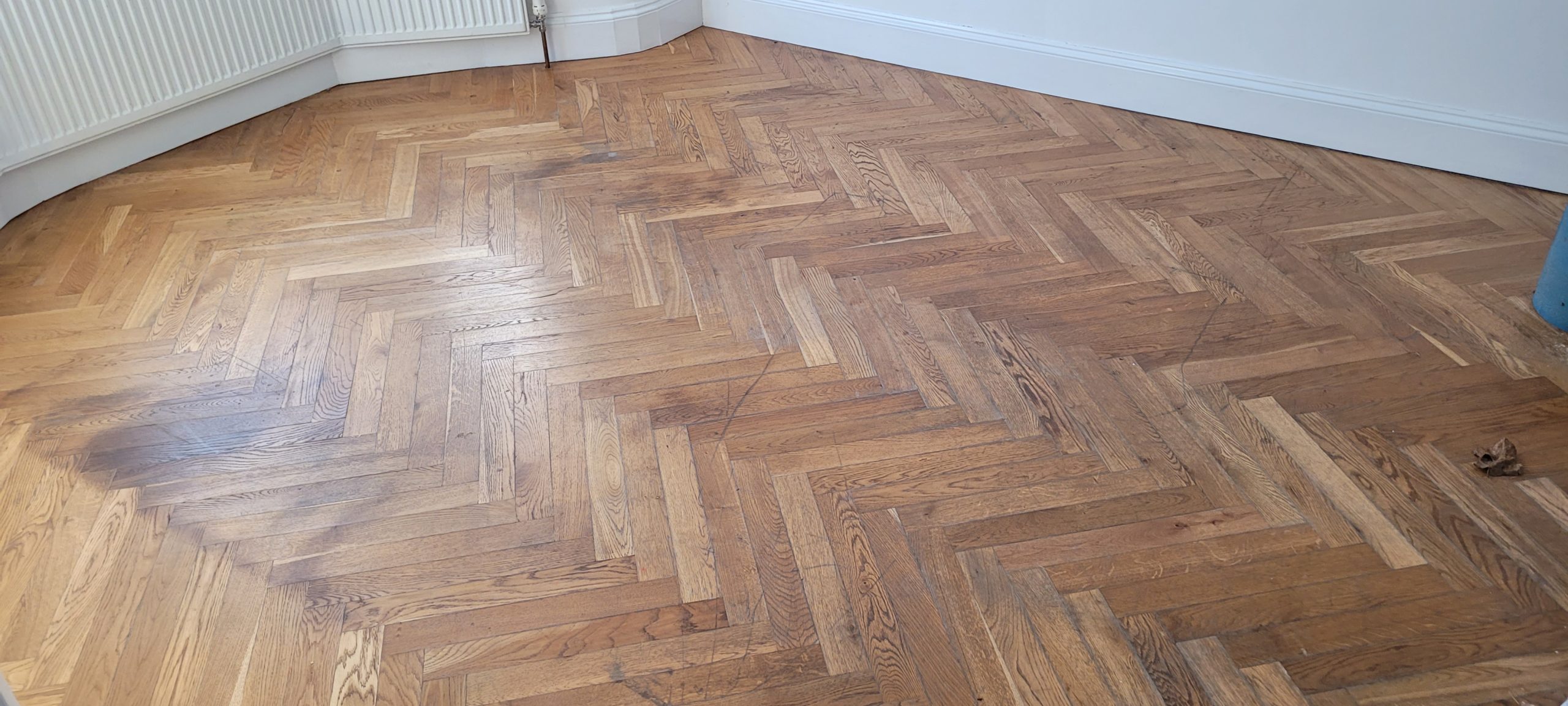 Worn oak herringbone parquet wood floor showing scuffs and dark patches before Herringbone Parquet Sanding in East Barnet.