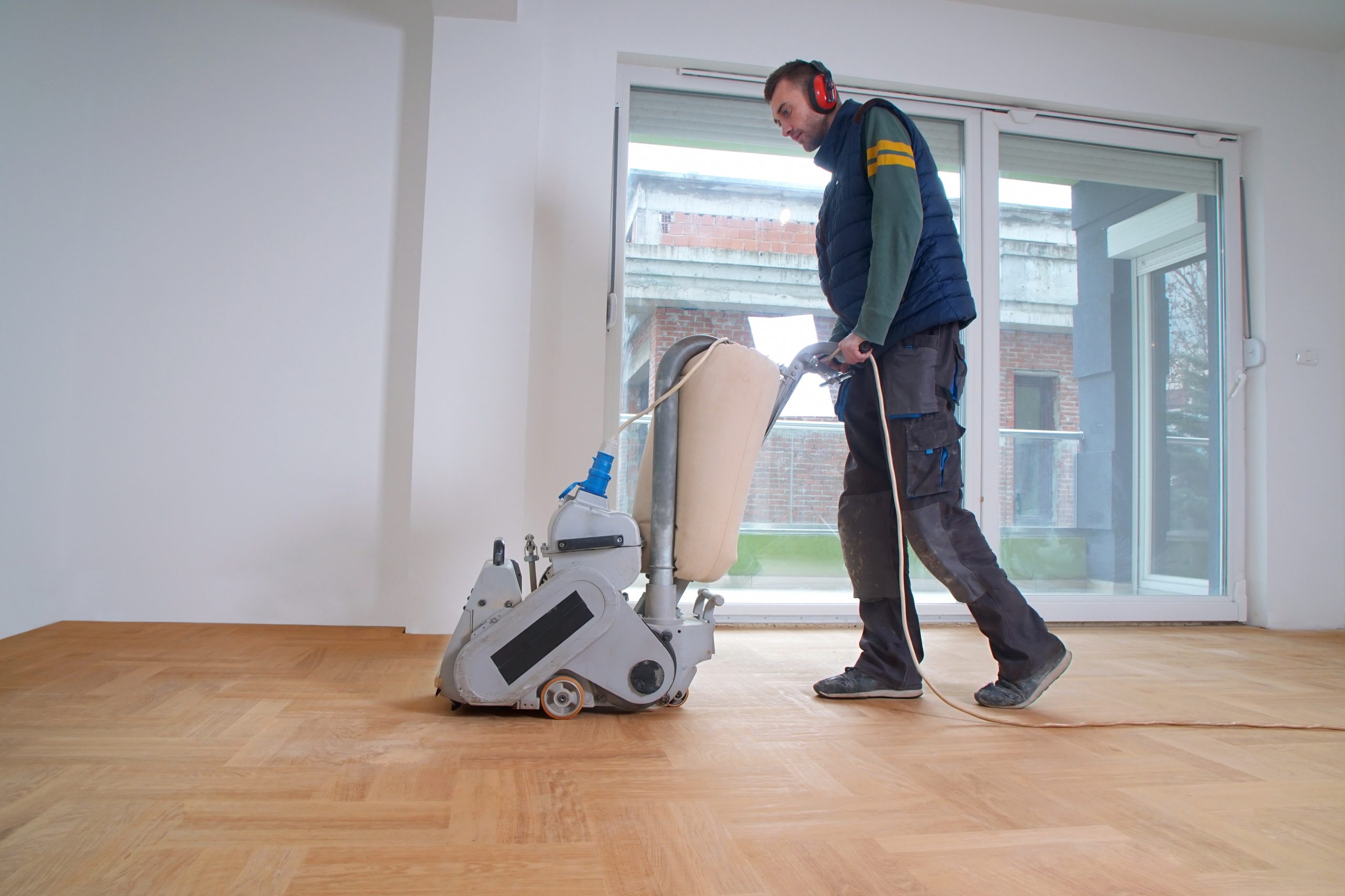 Professional using a belt sander on an oak herringbone parquet wood floor — Herringbone Parquet Sanding in East Barnet, bright living room with large sliding doors.