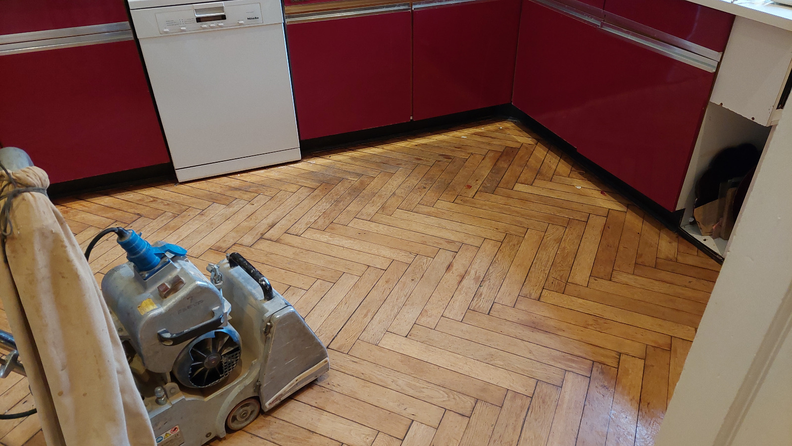 Wood Floor Sanding in eastbarnet on an oak herringbone parquet kitchen floor, with a professional belt sander ready to restore the worn blocks.