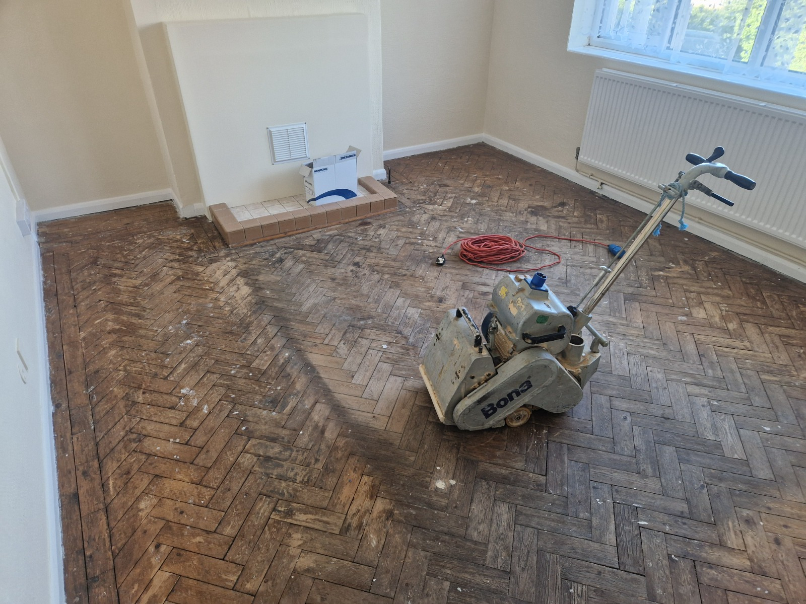 Wood Floor Sanding in eastbarnet on an old oak herringbone parquet living room floor, with a Bona sanding machine starting to strip back the dark, worn surface.