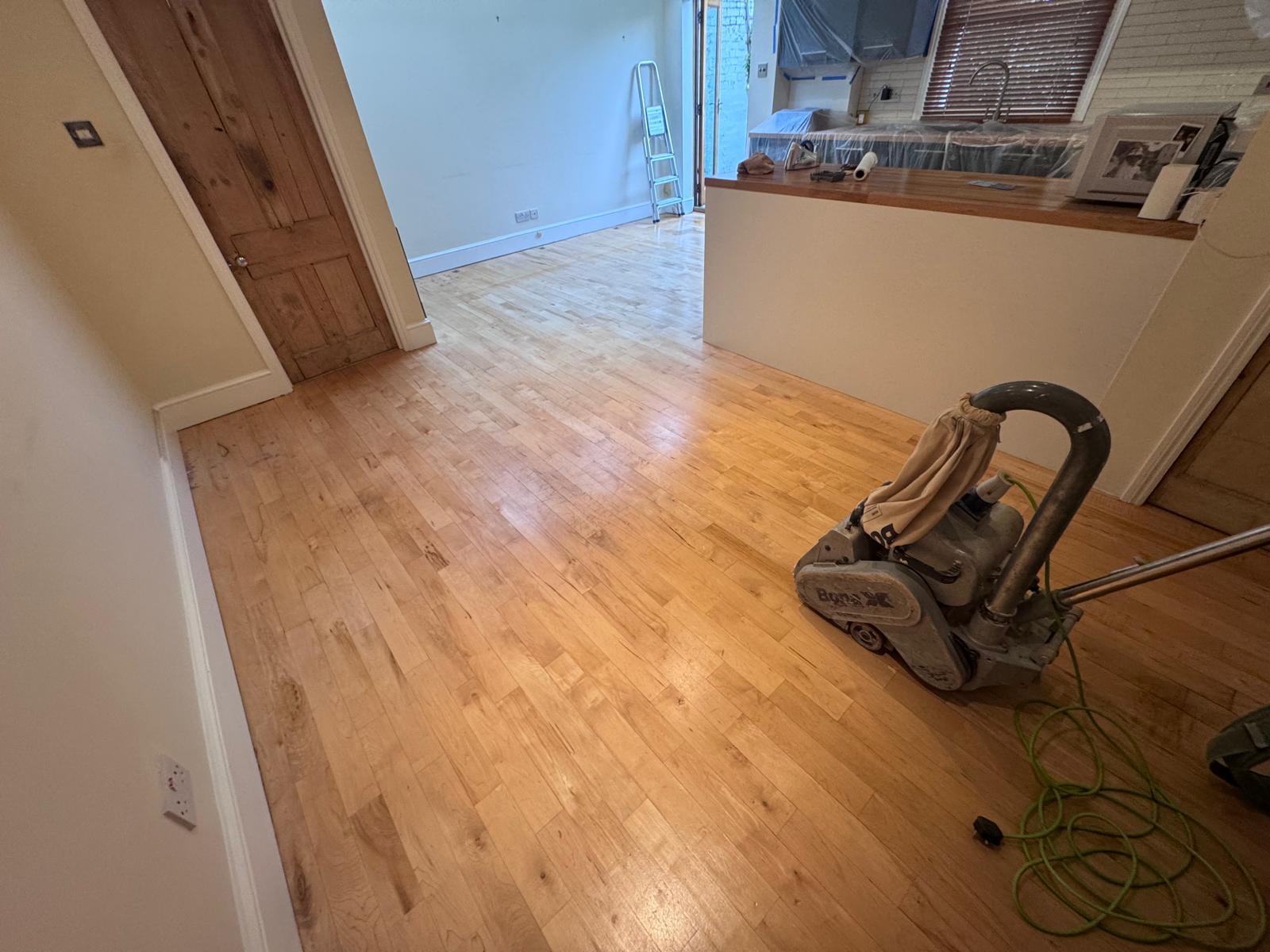 Hardwood Floor Sanding in eastbarnet on a light oak hardwood strip floor in an open-plan living room and kitchen, mid-sanding with professional machine.